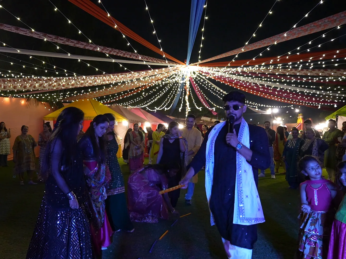 Ashish on the mic among dancers under the string-light canopy