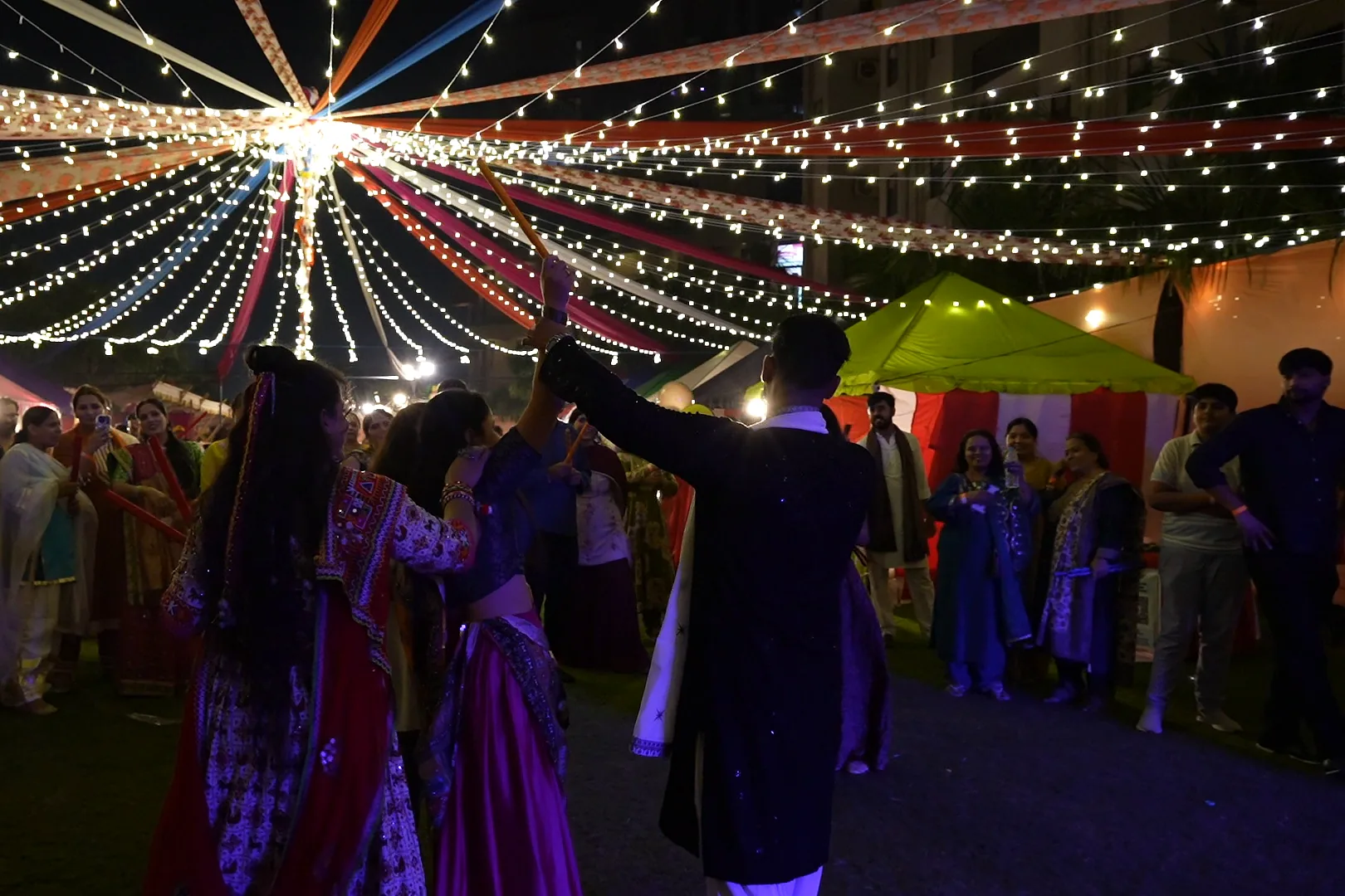 Ashish raises his arm to the ring of guests under the string-light canopy